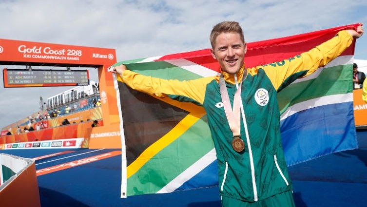 South Africa's Henri Schoeman poses with his country's flag after winning the men’s triathlon final during the 2018 Gold Coast Commonwealth Games at the Southport Broadwater Parklands venue in Gold Coast on April 5, 2018. / AFP PHOTO / ADRIAN DENNIS