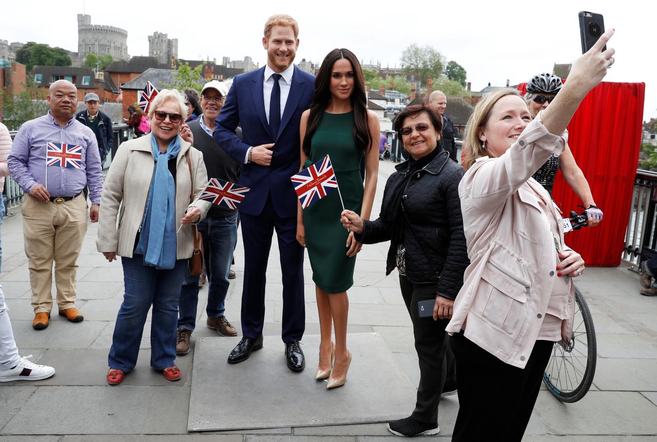 People pose for pictures and selfies with models of Britain's Prince Harry and Meghan Markle ahead of their wedding, in Windsor, Britain May 16, 2018.