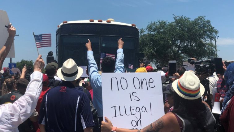 People protest in front of a bus carrying migrants near McAllen Detention Facility.
