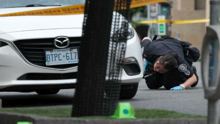 A police officer looks for evidence under a car while investigating a mass shooting on Danforth Avenue in Toronto, Canada.