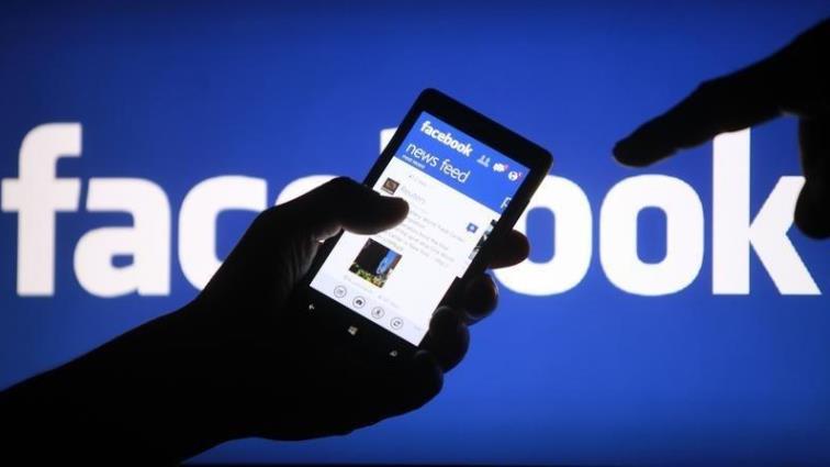 Cellphone on hand, Facebook logo on the background