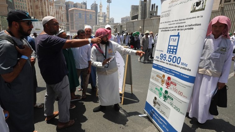 A translator helps pilgrims find information on a poster displaying helpful smartphone applications in the Saudi holy city of Mecca