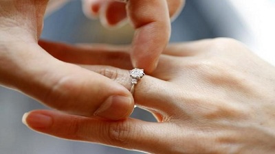 A man puts an engagement ring on a woman's finger during a photo opportunity.