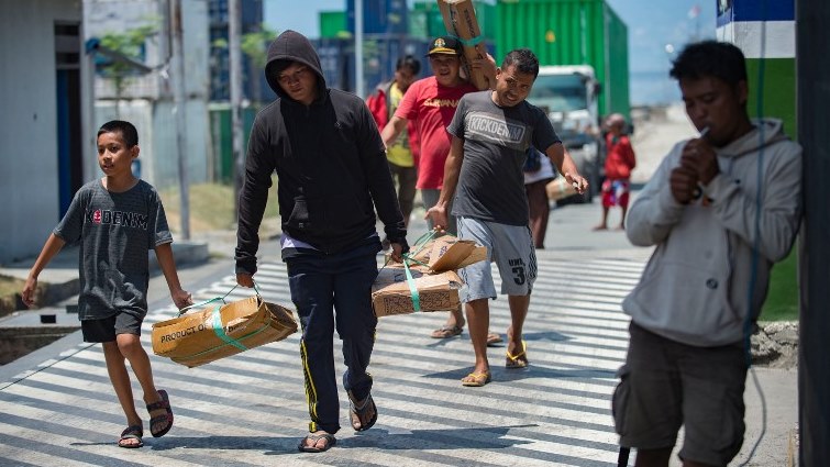 Quake-affected residents carry boxes of fish, distributed as aid by seaport officials, in Palu.