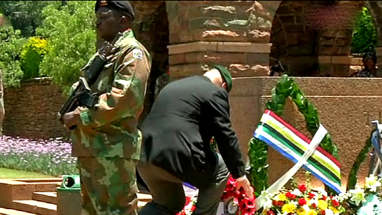 A man laying a wreath while a soldier stands guard