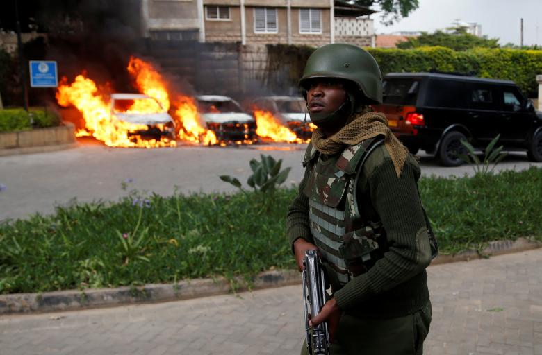A member of security forces walks as cars are seen on fire at the scene where explosions and gunshots were heard at the Dusit hotel compound, in Nairobi. REUTERS/Baz Ratner