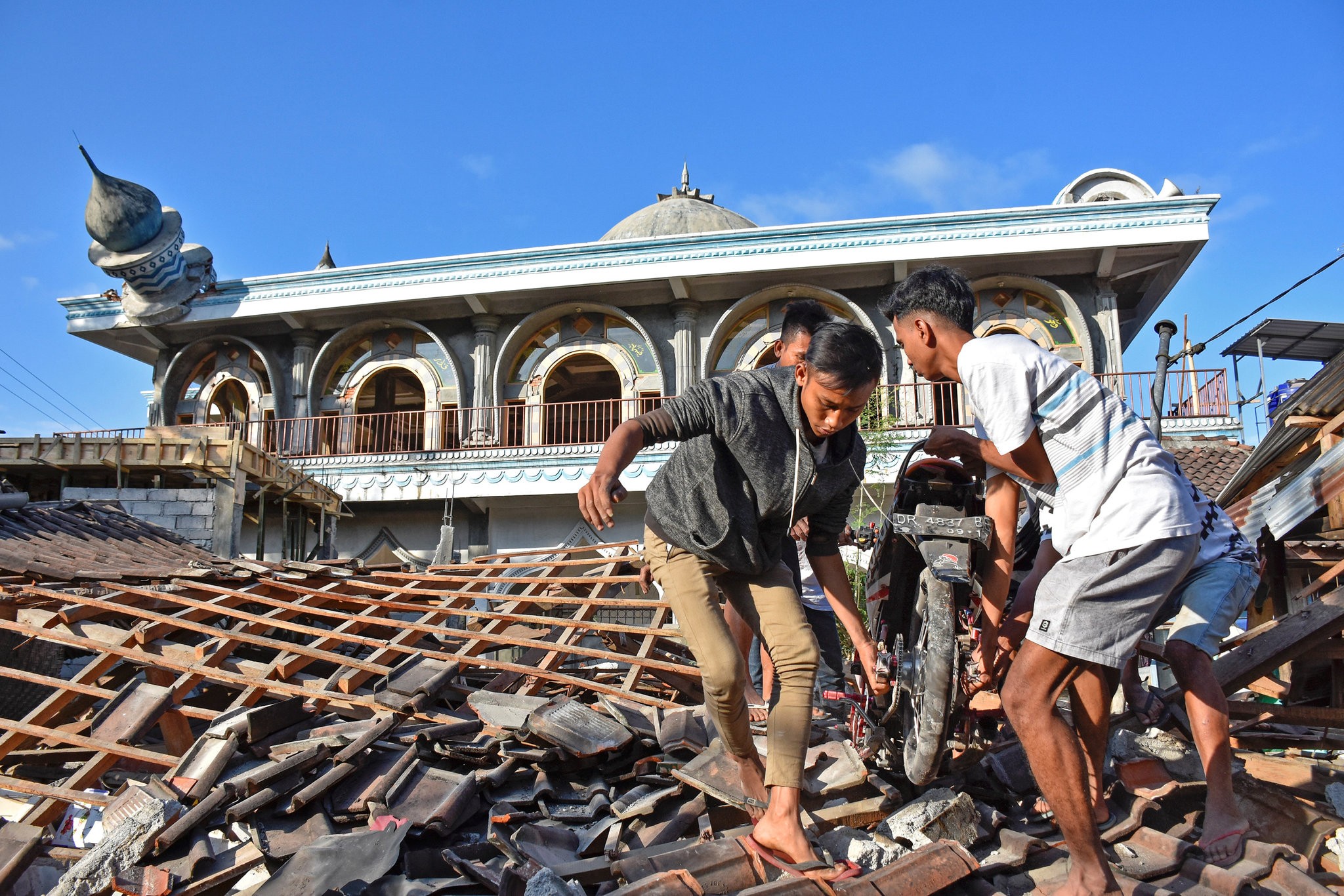 People in western Lombok, Indonesia, pulling a motorcycle from a damaged home near a mosque on Monday