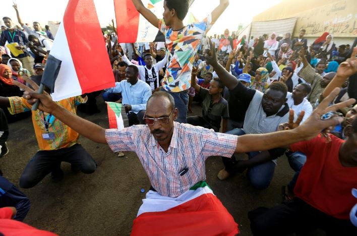 Sudanese demonstrators hold their national flag and chant slogans as they attend a mass anti-government protest outside Defence Ministry in Khartoum