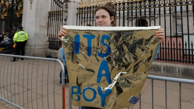 A woman holds a sign that reads "It's a boy" outside the gates of Buckingham Palace in London.