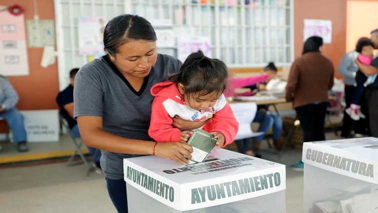 A voter carries a child as she casts her ballot at a polling station