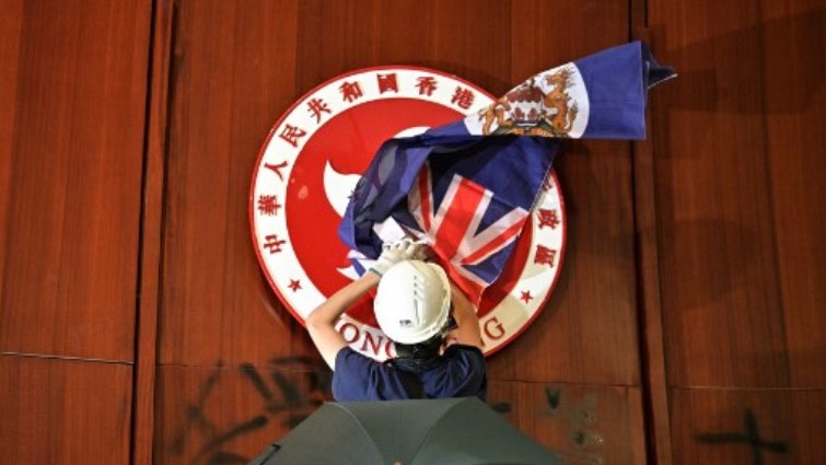 A protester attempts to cover the Hong Kong emblem with a British colonial flag after they broke into the government headquarters in Hong Kong.