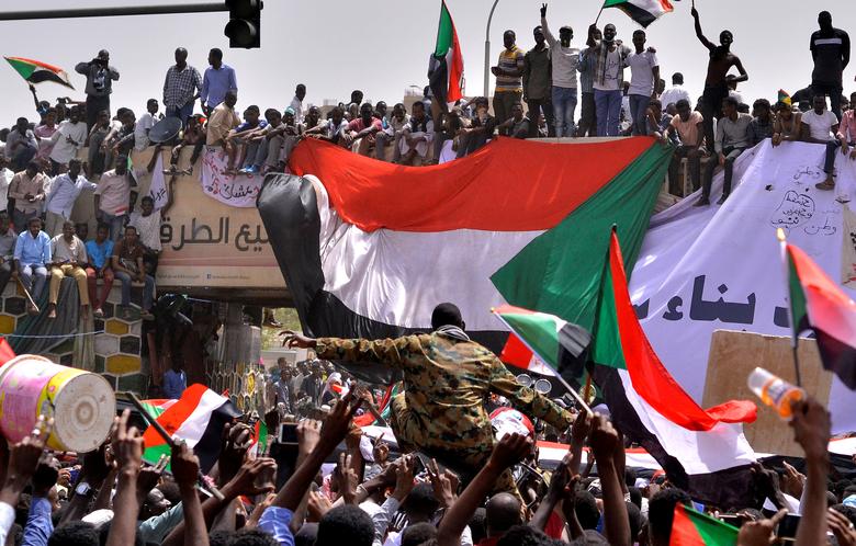 A military officer is carried by the crowd as demonstrators chant slogans and carry their national flags, after Sudan's Defense Minister said that President Omar al-Bashir had been detained 'in a safe place'.