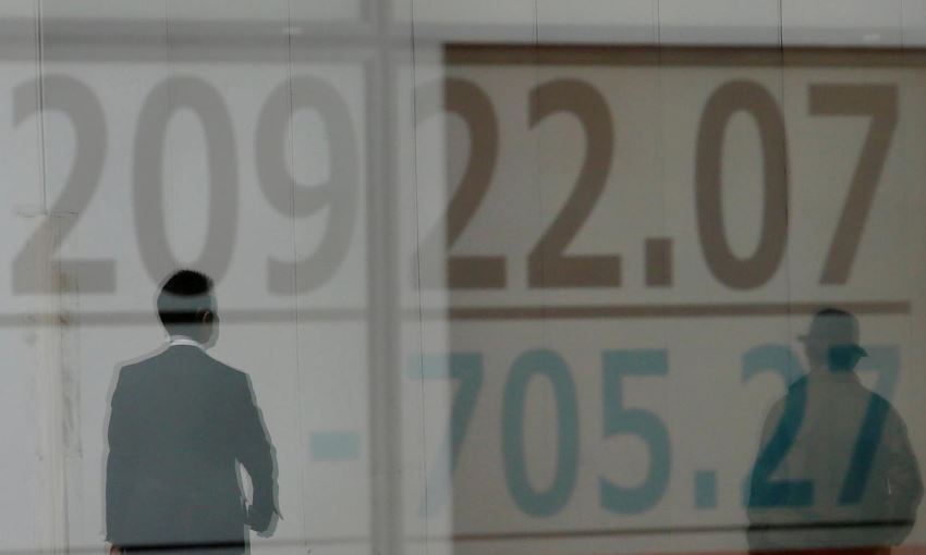 Men are reflected on an electronic board showing the Nikkei stock index outside a brokerage in Tokyo.