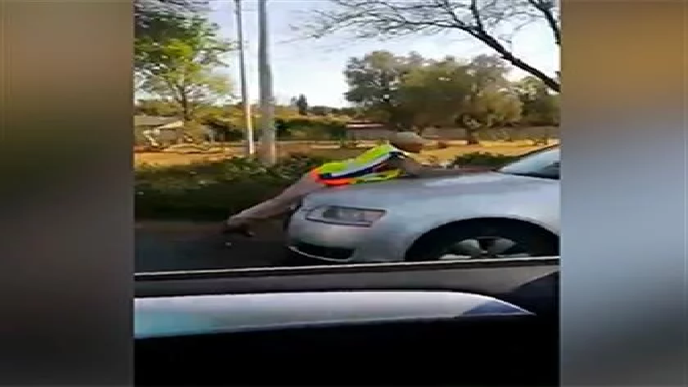 In a 17-second video - currently doing the rounds on social media, a police officer can be seen hanging on to the bonnet of a moving vehicle