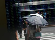 Passersby are reflected on a stock quotation board outside a brokerage in Tokyo, Japan.