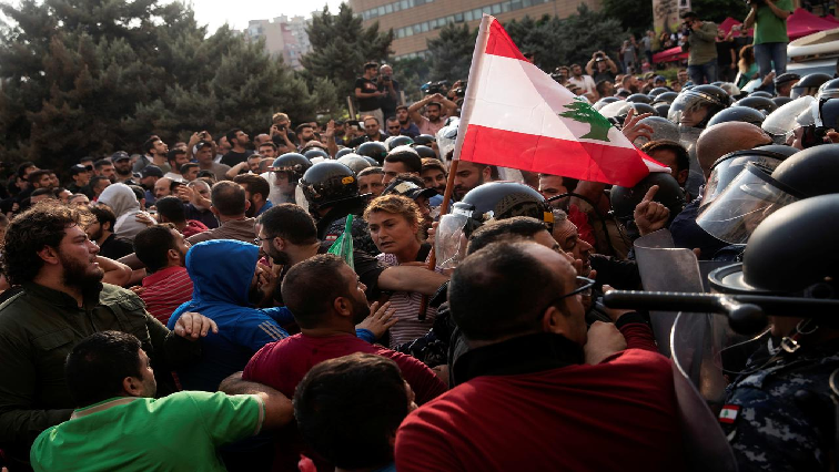 A woman holds a Lebanese flag as riot police confront Hezbollah supporters during ongoing anti-government protests in downtown Beirut, Lebanon.