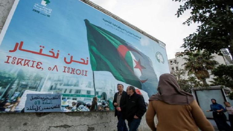 People walk past a campaign poster for presidential election in Algiers, Algeria.