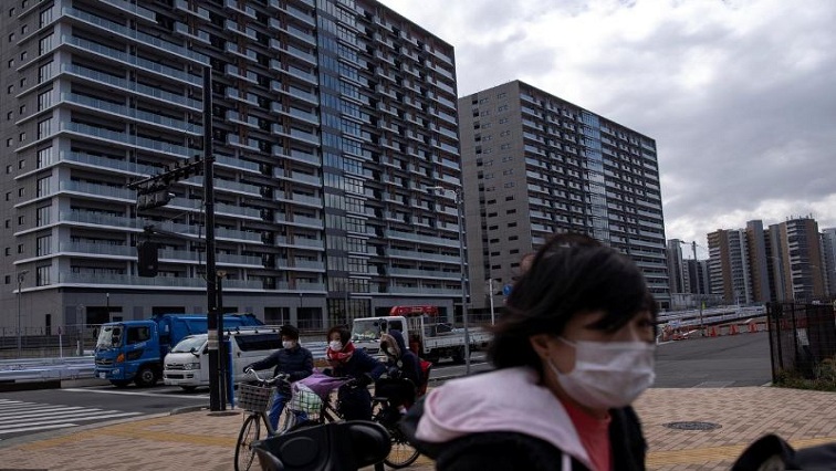 People wearing face masks, following an outbreak of the coronavirus, ride their bicycles past an under-construction site of the Tokyo 2020 Olympics villages in Tokyo, Japan.