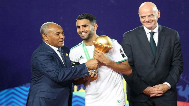 Algeria's Riyad Mahrez receives the trophy from CAF President Ahmad Ahmad after winning the Africa Cup of Nations in 2019 as FIFA President Gianni Infantino looks on.