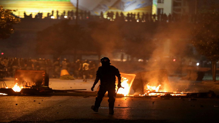 A member of the Lebanese riot police walks near a burning fire during a protest against the fall in pound currency and mounting economic hardship, in Beirut, Lebanon.