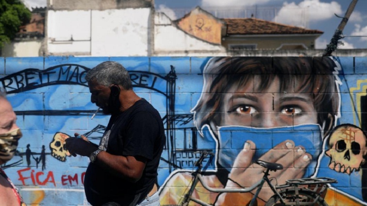 People wearing protective masks walk past a graffiti, following the coronavirus disease (COVID-19) outbreak, in Rio de Janeiro, Brazil.
