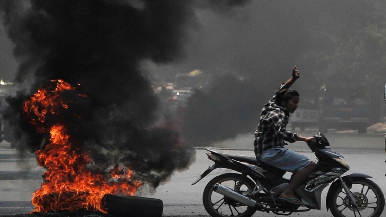 A man flashes the three-finger salute as he passes burning tires during a protest against the military coup, in Mandalay, Myanmar, on April 1, 2021.