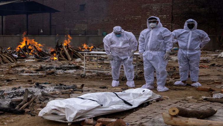 Men wearing protective suits stand next to the body of their relative, who died from the coronavirus disease (COVID-19), before her cremation at a crematorium ground in New Delhi, India.
