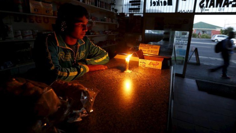 Shop owner sits next to a candle during power outage