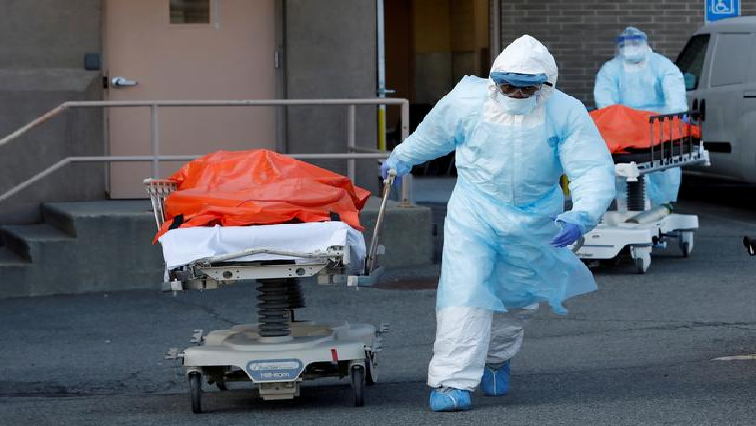 A healthcare worker dressed in personal protective equipment is seen pushing a body covered in plastic.