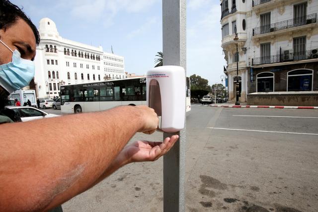 A man wearing a protective face mask uses a hand sanitizer dispenser on the street following the spread of the coronavirus disease (COVID-19), in Algiers, Algeria