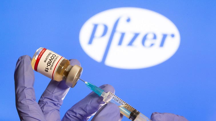 A woman holds a small bottle labeled with a "Coronavirus COVID-19 Vaccine" sticker and a medical syringe in front of displayed Pfizer logo in this illustration taken, on October 30, 2020.