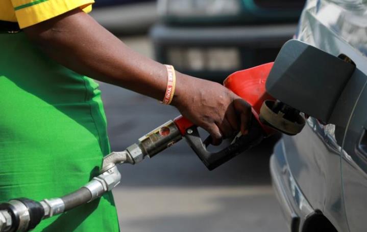 A worker holds a nozzle to pump petrol into a vehicle at a fuel station.