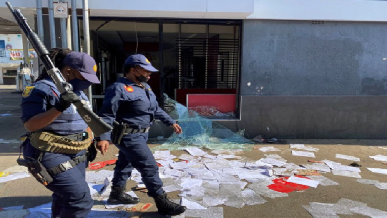 Police walk past a shop looted in protests following the jailing of former president Jacob Zuma, in Durban.