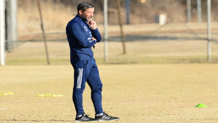 Orlando Pirates coach, Josef Zinnbauer, is seen standing on a soccer field.