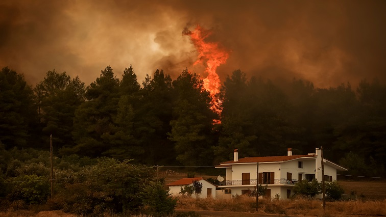 Flames rise near a house as a wildfire burns in the village of Kirinthos, on the island of Evia, Greece