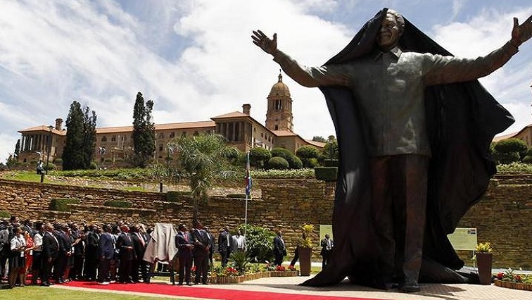 People stand near the 9-metre (30-feet) bronze statue of the late former South African President Nelson Mandela as it is unveiled as part of the Day of Reconciliation Celebrations at the Union Buildings in Pretoria December 16, 2013.
