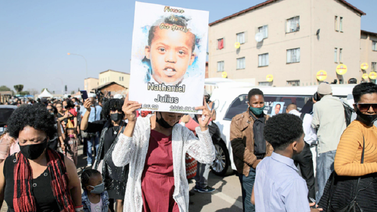 A resident holds a placard with a picture of 16-year-old Nathaniel Julies at his funeral in Eldorado Park.