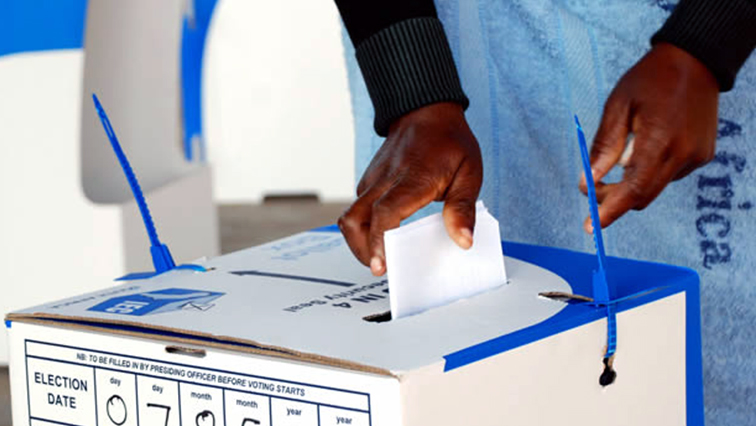A person pushes in their ballot paper into a ballot box after casting their vote.