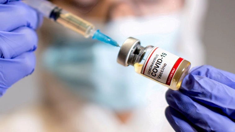 A woman holds a small bottle labelled with a "Coronavirus COVID-19 Vaccine" sticker and a medical syringe in this illustration.