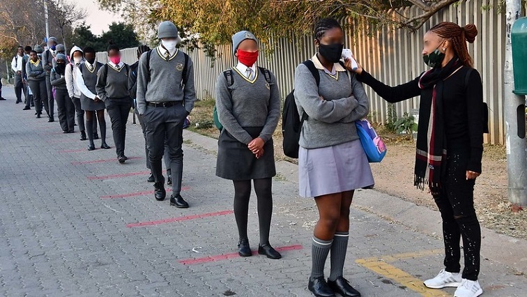 [File Image] School learners line up and social distance while getting screened.
