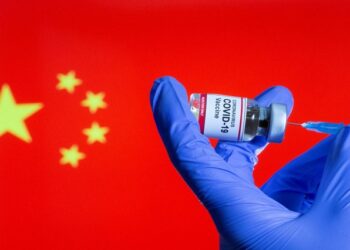 A woman holds a small bottle labeled with a "Coronavirus COVID-19 Vaccine" sticker and a medical syringe in front of displayed China flag in this illustration taken, October 30, 2020.