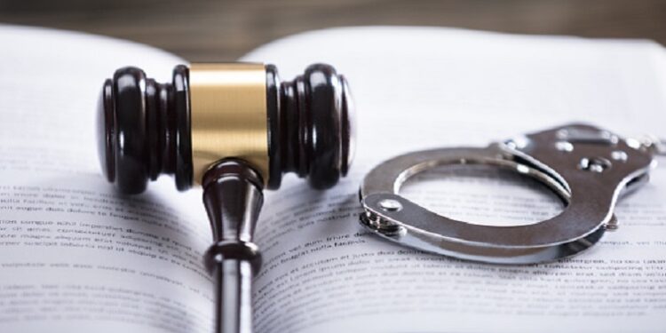 Close-up of gavel and handcuffs on a law book in a courtroom.