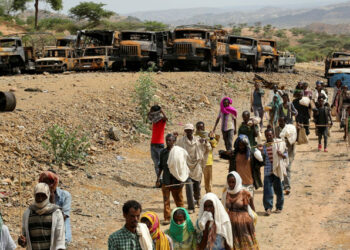 Villagers return from a market to Yechila town in south central Tigray walking past scores of burned vehicles, in Tigray, Ethiopia, July 10, 2021.