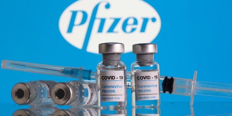 Vials labelled "COVID-19 Coronavirus Vaccine" and sryinge are seen in front of displayed Pfizer logo in this illustration taken, February 9, 2021.