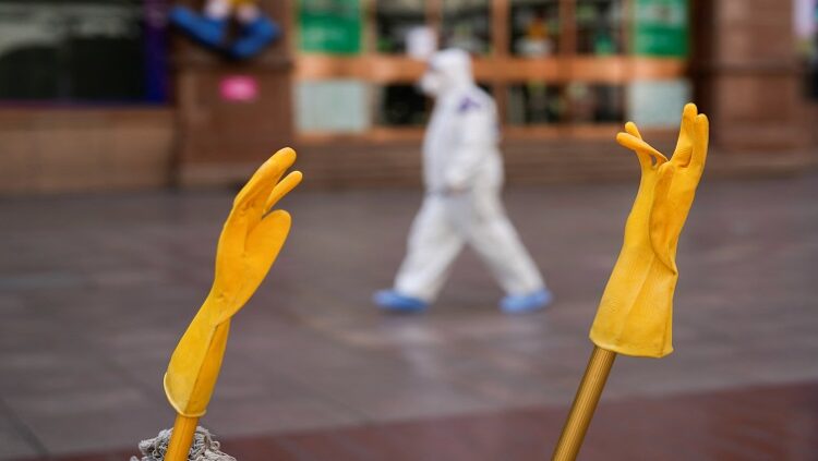 A pair of rubber gloves is hung to dry, as a security guard in personal protective equipment (PPE) walks along a street, following the coronavirus disease (COVID-19) outbreak in Shanghai, China