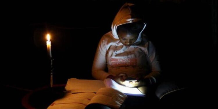 Thandiwe Sithole looks at her mobile phone as she studies by a candle light during one of frequent power outages from South African utility Eskom