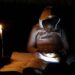 A learner looks at her mobile phone as she studies by a candle light during one of frequent power outages from South African utility Eskom