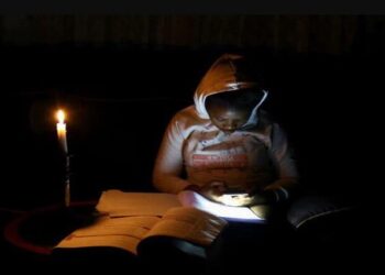 Thandiwe Sithole looks at her mobile phone as she studies by candlelight during one of the power outages, March 2022