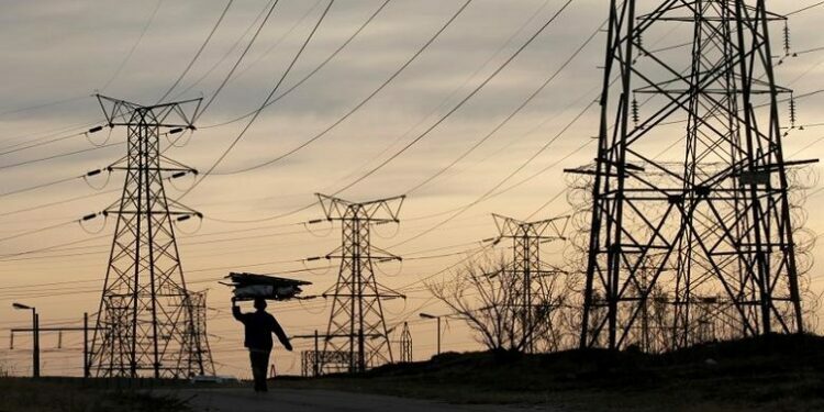 File image: A woman carries fire wood on her head as she walks below Eskom's electricity pylons in Soweto.
