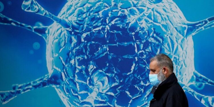 A man wearing a protective face mask walks past an illustration of a virus, August 3, 2020.